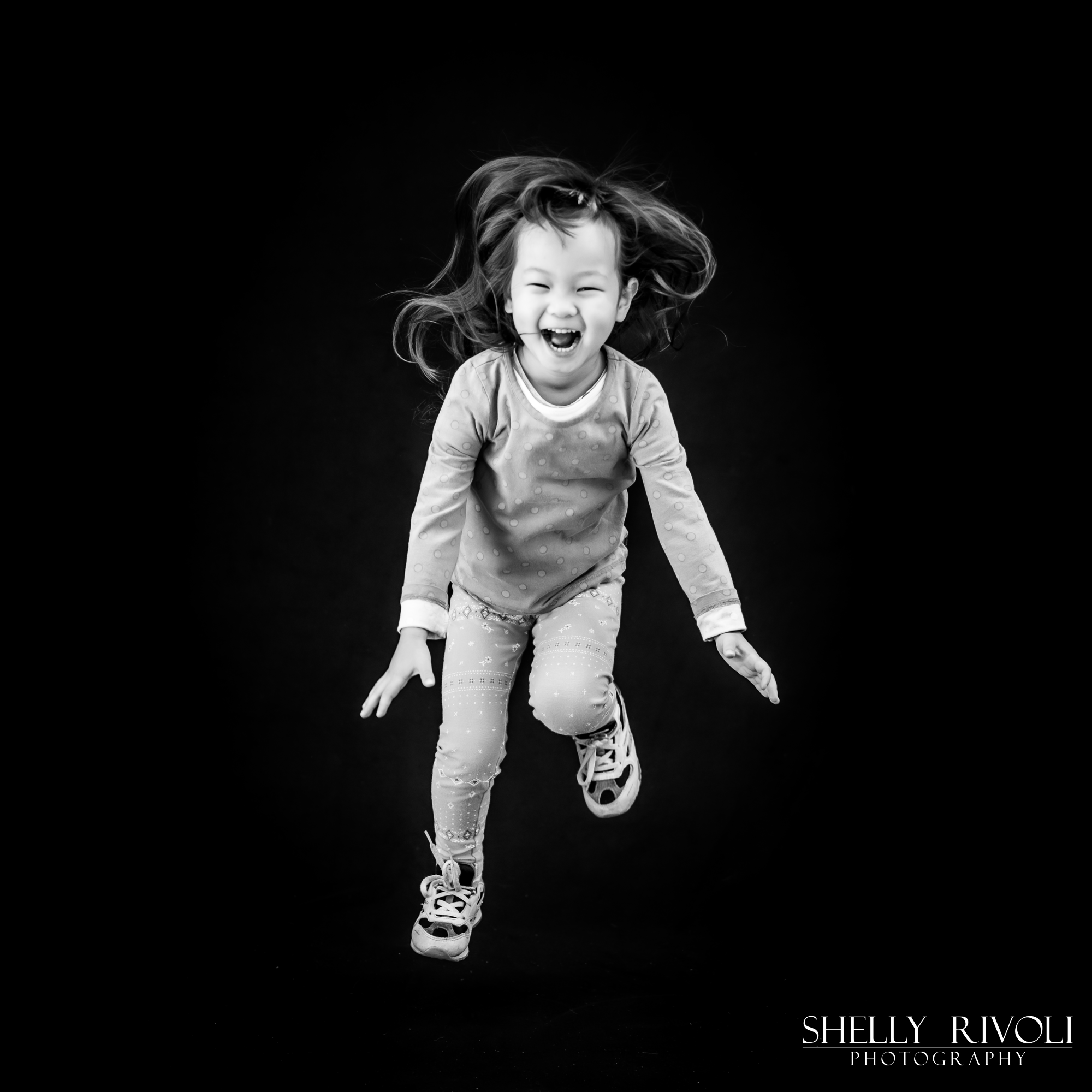A laughing girl jumps in air during a children's portraits session