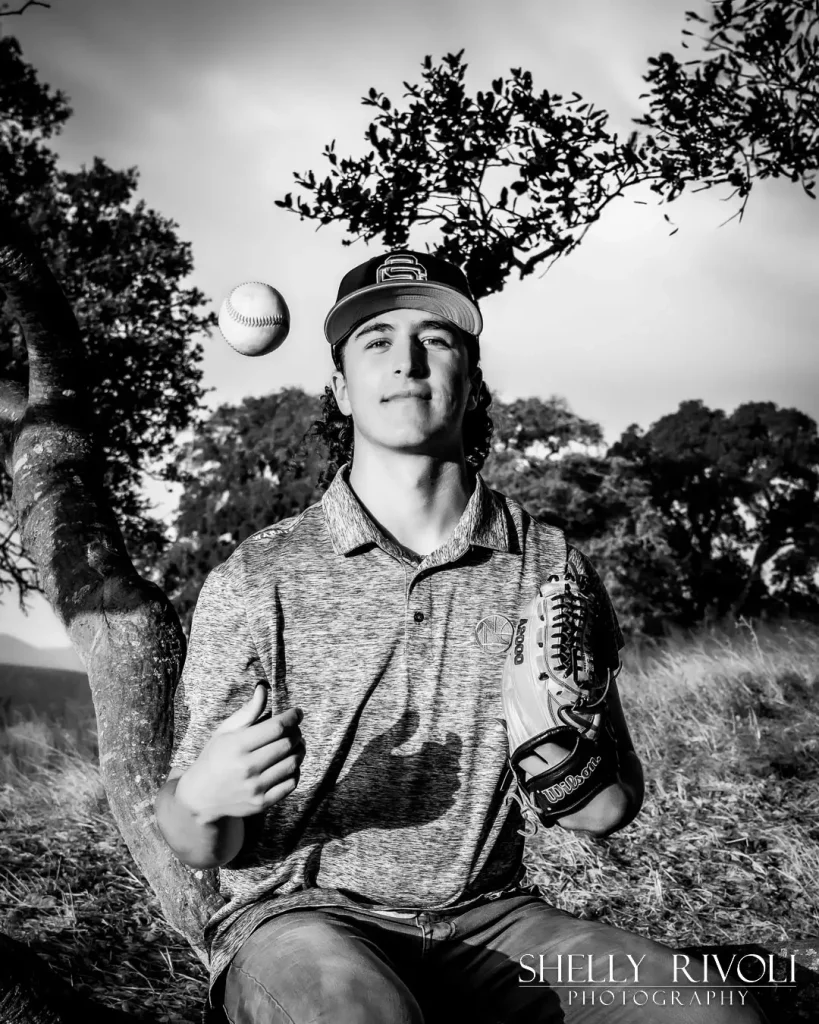 BW outdoor senior portrait of baseball player tossing ball